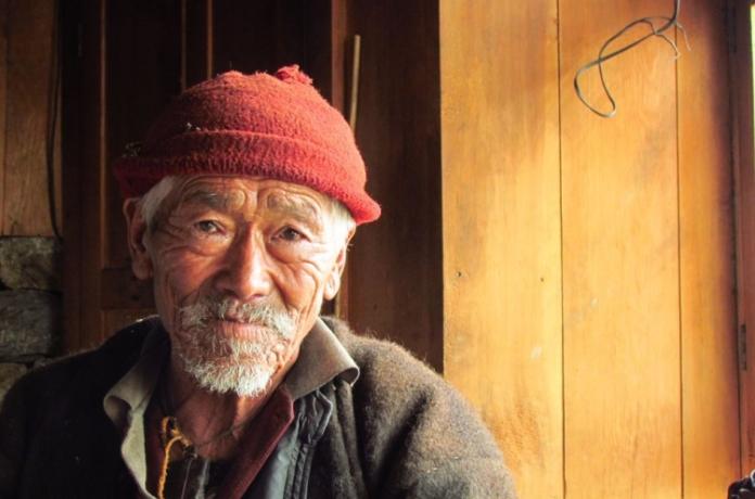 Alter Mann mit Mütze lächelt vor Holzwand