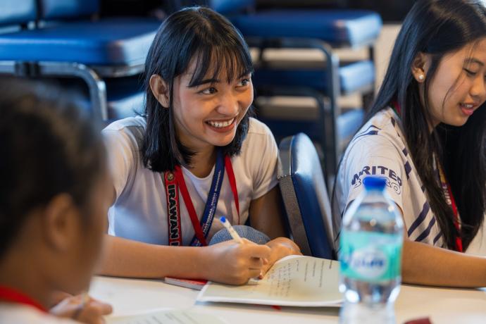 Young girl smiles as she writes in her notebook.