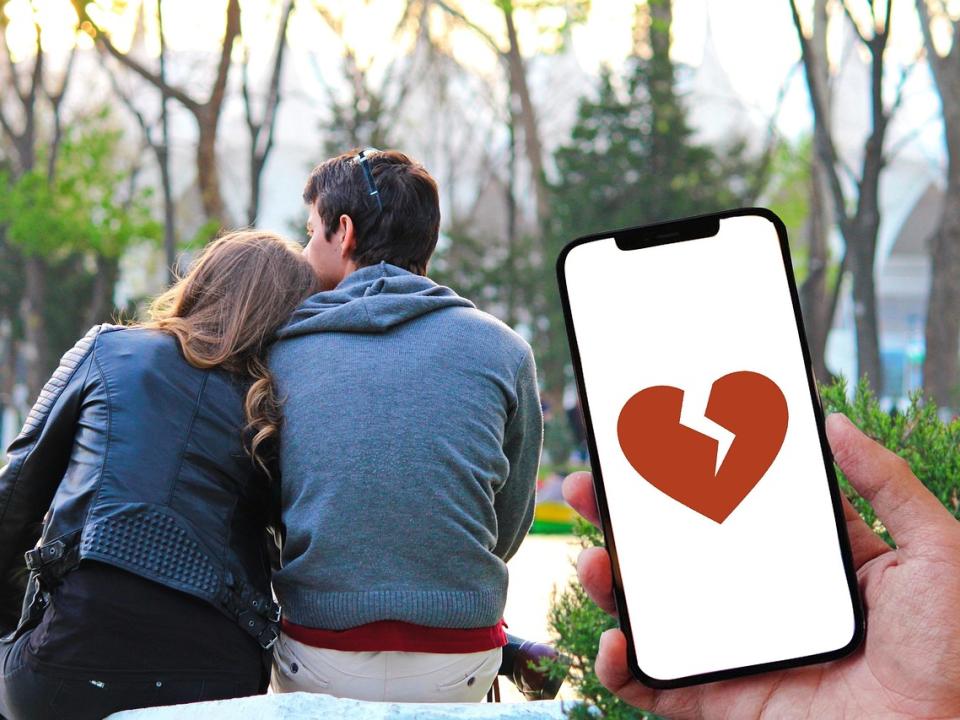 coppia visto di schiena, con in primo piano un cellulare che mostra un cuore rotto