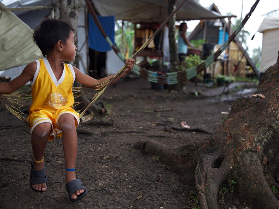 Little boy looks back for his father as he swings on the hammocks of his new home in a tent village following Typhoon Haiyan