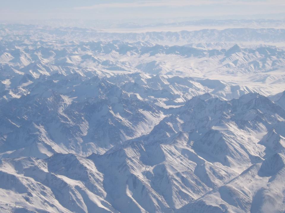 Multiple ranges of snow-covered mountains in Central Asia stretch off into the distance.