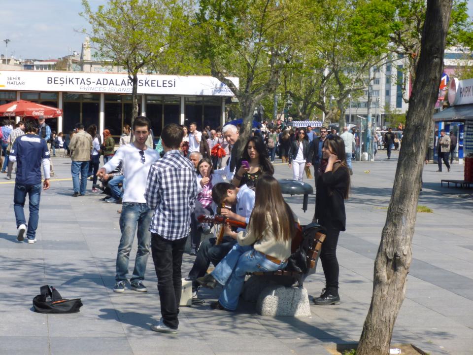 In an open area in Istanbul people wander past or gather in groups.