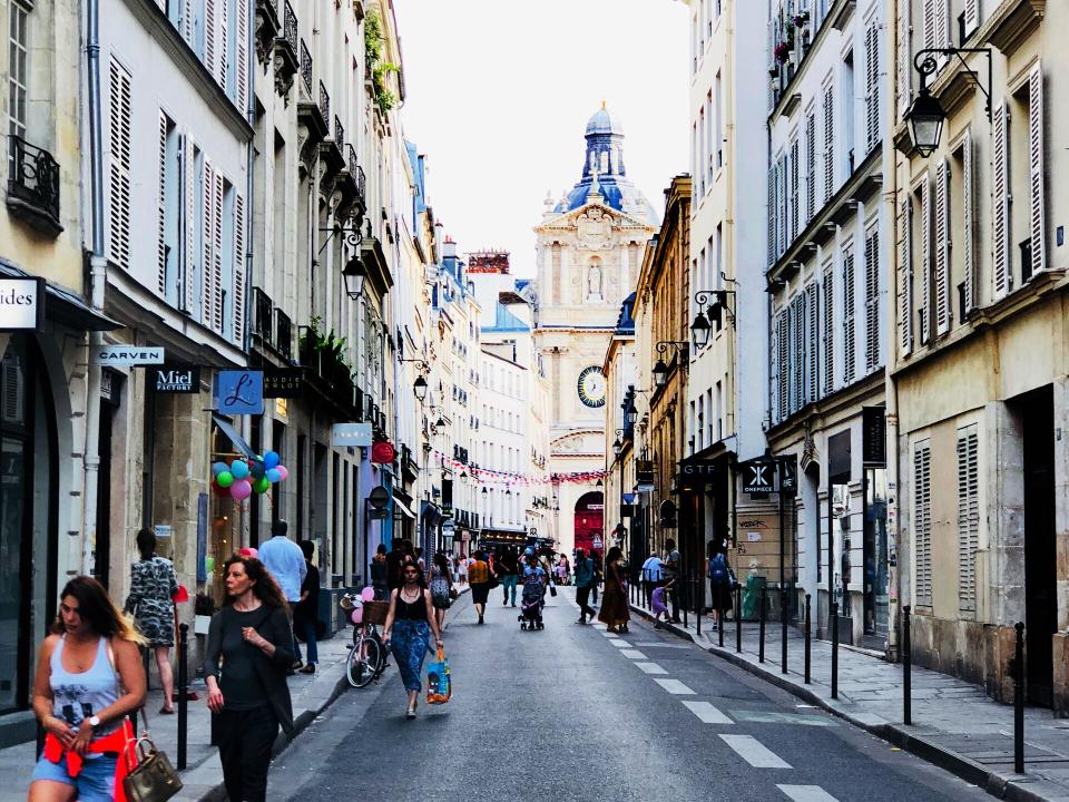 A narrow street in the center of Paris, lined with cafes, boutiques, and flower shops
