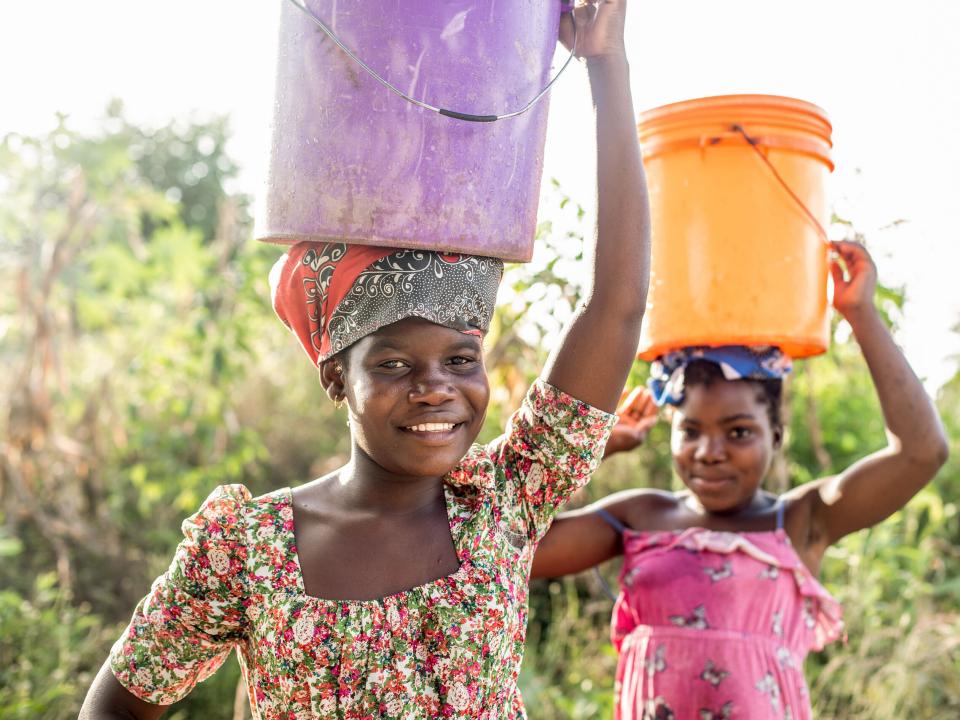 Two girls balance water buckets on their heads as they walk in Mozambique. Photo by Rebecca Rempel.