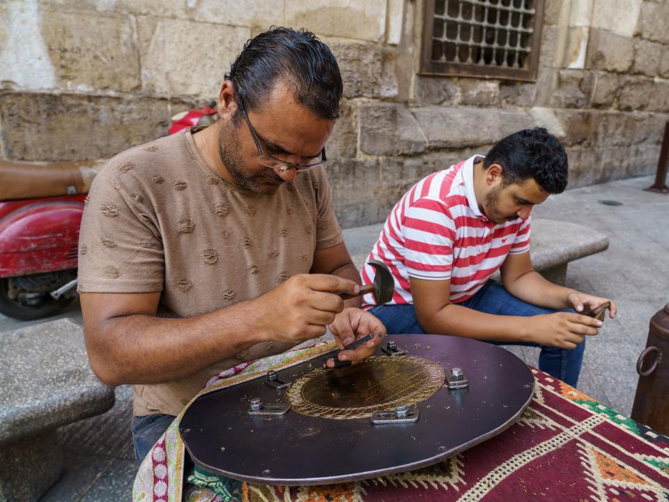 Artisan crafts ornate designs on brass to sell at his shop on the streets of North Africa.  Image by Garrett N