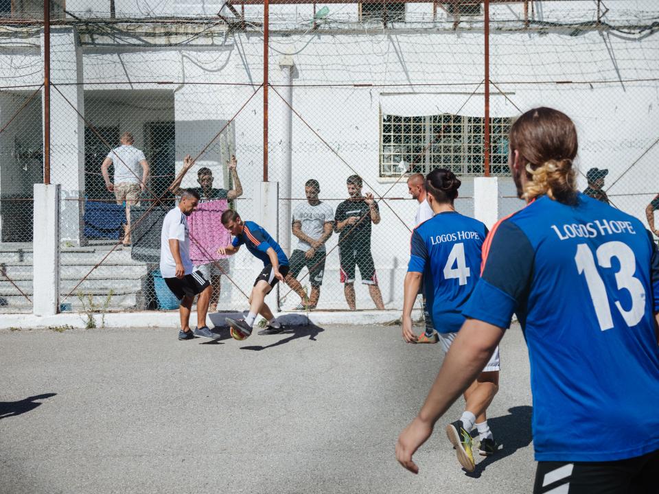 Vlore, Albania :: Crewmembers play football with the inmates in a prison.
