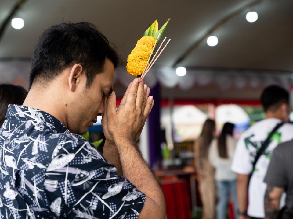 Man holding yellow flowers prays at a Buddhist shrine in Thailand. Photo by Rebecca Rempel.