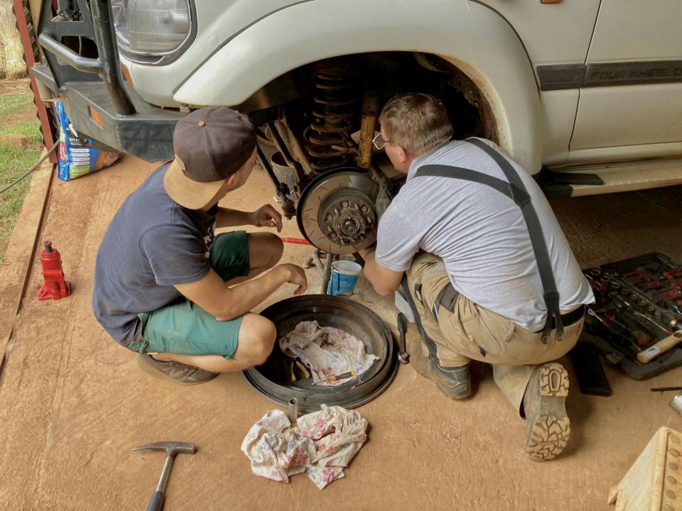 In a makeshift workshop nestled in rural Africa, a seasoned mechanic imparts his knowledge to an eager apprentice. Together, they diligently use basic tools to repair a lifted 4x4 Landcruiser, showcasing community-driven skill development. Photo by Christ