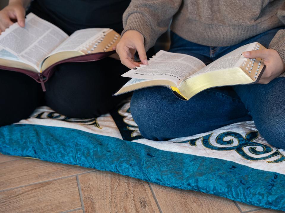 A group of young women sit together on a floor cushion and read the Bible in Central Asia. Photo by RJ Rempel.