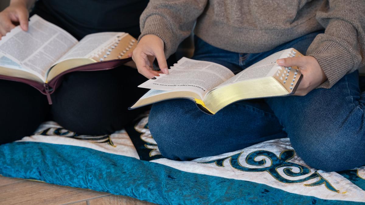 A group of young women sit together on a floor cushion and read the Bible in Central Asia. Photo by RJ Rempel.