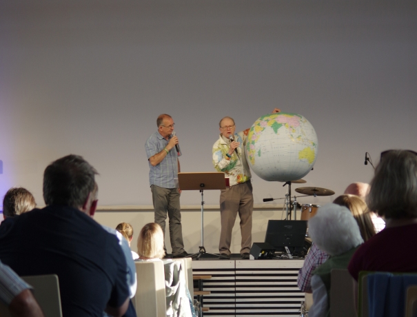 George Verwer predigt in Wetzlar und hält dabei eine aufblasbare Weltkugel in der Hand