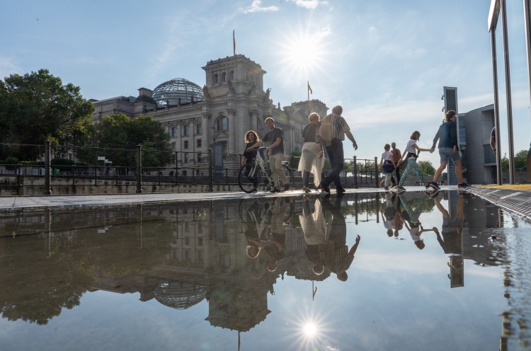 Menschen vor dem Reichstagsgebäude spiegeln sich in einer Pfütze
