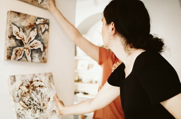 Female artist reaches for artwork on the wall to adjust position